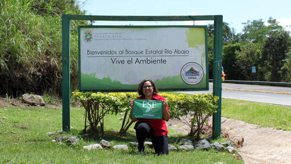 A woman stands holding a green flag, smiling and looking at the camera.